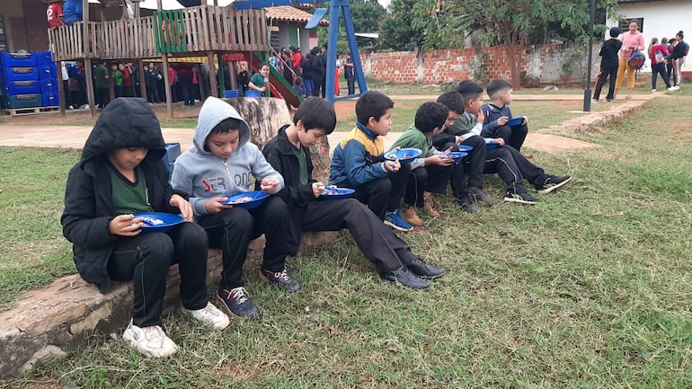 En un ambiente improvisado, y valiéndose de un muro que servirá de cimiento para unas aulas, y los regazos de los niños sirvieron para que los escolares se puedan alimentar.