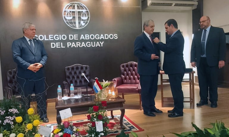 El doctor Manuel Riera Escudero recibe la distinción de manos de su hijo Manuel Riera. El ministro del Interior, Enrique Riera (izq.) y el presidente del Colegio de Abogados, Jorge Arturo Daniel, observan la escena.