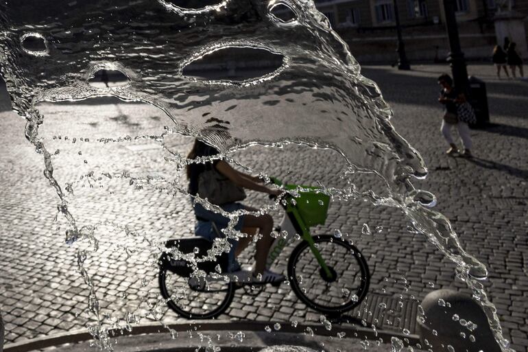 Una mujer en bicicleta cruza frente a una fuente de agua en Roma, Italia, este martes.