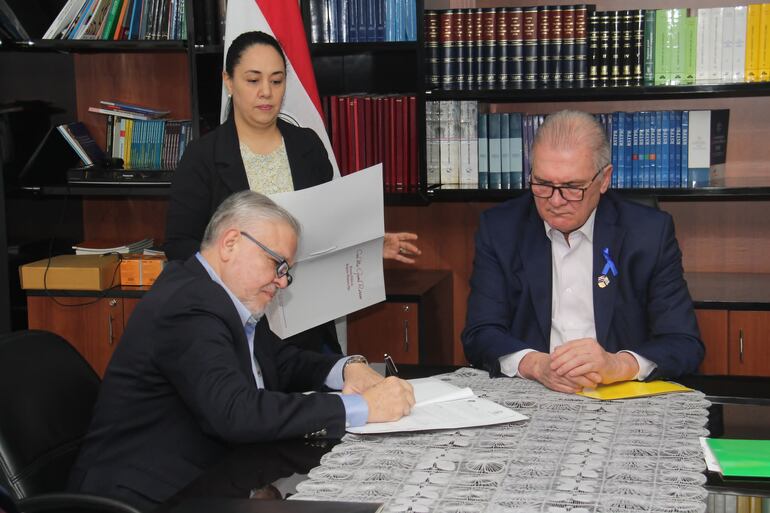 El presidente del IPS, Jorge Brítez (izq), firmando el acuerdo junto al fiscal general del Estado, Emiliano Rolón (der)., donde estipulan el pago de deuda por inmueble mediante acuerdo extrajudicial