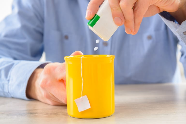 Una persona endulza una taza de te con edulcorante.