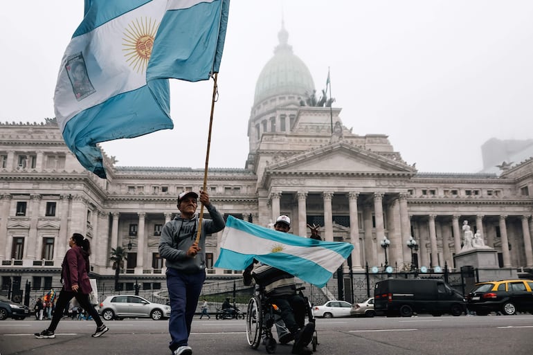 Personas sostienen banderas a las afueras del senado argentino.