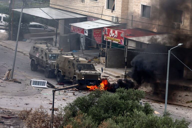 TOPSHOT - Tyres burn beneath Israeli security forces armoured vehicles during a raid in Jenin in the occupied West Bank on June 19, 2023. Israeli forces in the occupied West Bank killed three Palestinians, in a raid that saw seven Israeli security personnel wounded and rare helicopter fire as the army said it pursued "wanted suspects". (Photo by Jaafar ASHTIYEH / AFP)