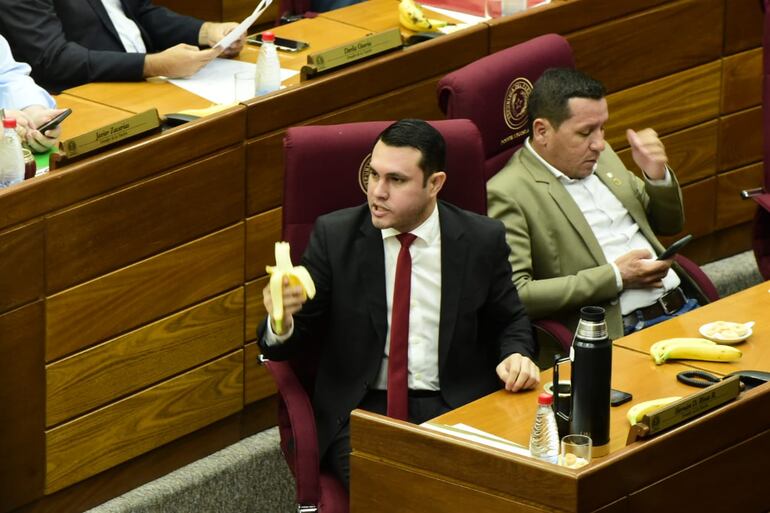 El senador cartista Hernán Rivas come una banana mientras se vota su desafuero. A su lado, su colega Javier "Chaqueñito" Vera se distrae con el celular.