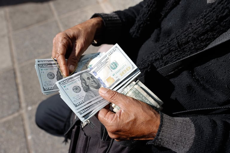 Fotografía de un cambista informal sosteniendo dólares este viernes en el centro de Asunción (Paraguay). El alza del dólar, atribuido por expertos a una demanda estacional y un "drenaje" de billetes verdes hacia BoliviaEFE/ Juan Pablo Pino