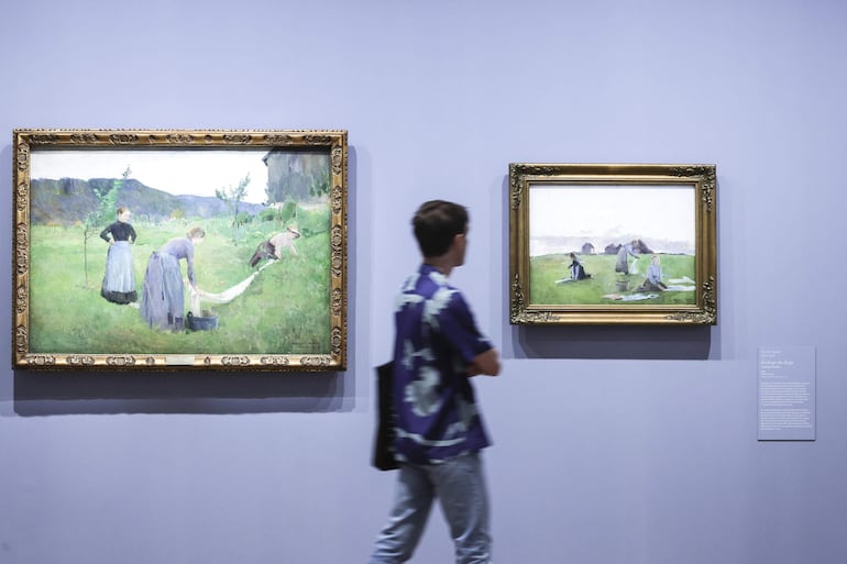 Un hombre camina junto a las pinturas 'el campo blanqueador' y 'ropa seca' de Harriet Backer durante la gira de prensa de la exposición 'Harriet Backer. La música de los colores' en el Museo de Orsay en París, Francia.