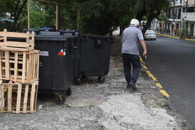 Sobre Azara y Constitución, centro de Asunción, un hombre circula con dificultad entre las veredas rotas, cajas y contenedores municipales.