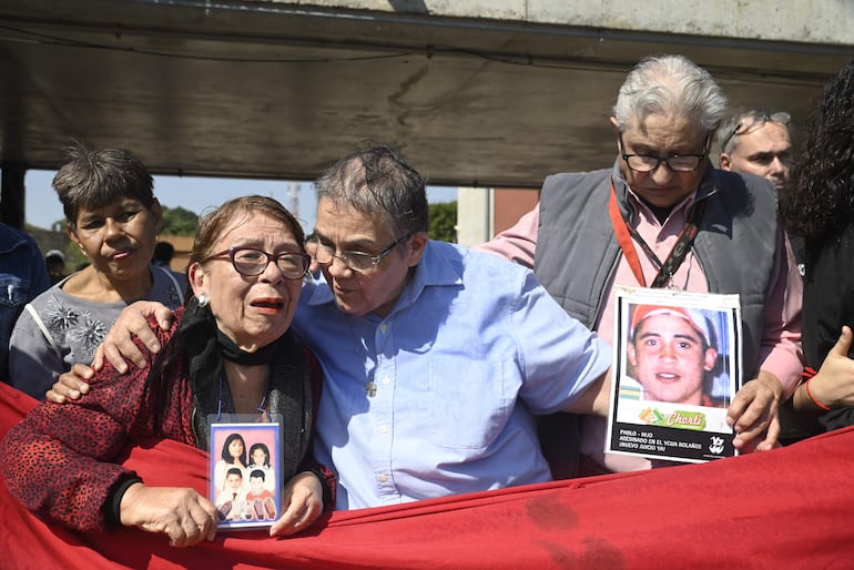 Juan Dionisio Torres (derecha) con la fotografía de su hijo Pablo, comparte con otros familiares y sobrevivientes del Ycua Bolaños, en el despliegue de la bandera simbólica.