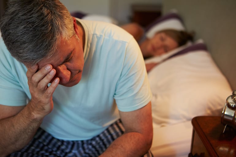 Hombre estresado al costado de la cama.