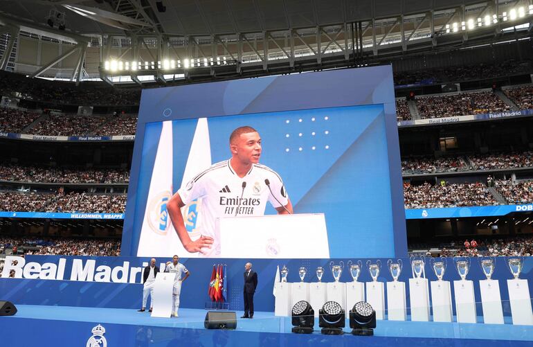 French forward Kylian Mbappe delivers a speech on stage next to Real Madrid's President Florentino Perez (R), Real Madrid's Honorary President Jose Martinez Pirri and French former football player Zinedine Zidane (L) during his first appearance as a Real Madrid player at Santiago Bernabeu Stadium in Madrid on July 16, 2024, after signing his new five-season contract. Still celebrating Spain's Euro 2024 triumph, Real Madrid fans have even more to cheer this July 16, 2024, as French superstar Kylian Mbappe is officially presented to a packed-out Santiago Bernabeu stadium. (Photo by Pierre-Philippe MARCOU / AFP)