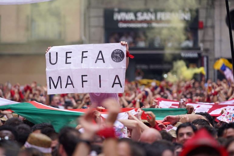 A participant holds a banner reading "UEFA Mafia" during the "Chupinazo" (start rocket) opening ceremony to mark the kick-off of the San Fermin bull Festival outside the Town Hall of Pamplona in northern Spain on July 6, 2023. Thousands of people every year attend the week-long festival and its famous 'encierros': six bulls are released at 8:00 a.m. evey day to run from their corral to the bullring through the narrow streets of the old town over an 850 meters (yard) course while runners ahead of them try to stay close to the bulls without falling over or being gored. (Photo by CESAR MANSO / AFP)