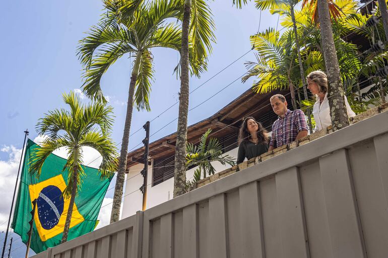 Claudia Macero (i), Pedro Uchurrurtu (c) y Magalli Meda, asilados en la residencia del embajador de Argentina, saludan a los medios de comunicación desde un balcón con la bandera de Brasil a un costado en Caracas (Venezuela).