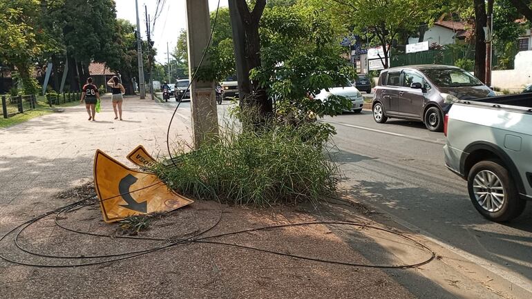 Un cartel del MOPC desplazado por una columna en el suelo con yuyos.