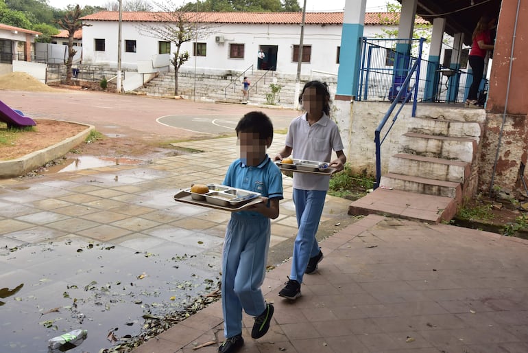 Estudiantes caminan una larga distancia desde que les sirven la bandeja del almuerzo hasta llegar a sus salas de clase en la escuela Juan Pedro Escalada de Lambaré, donde no tienen comedor.