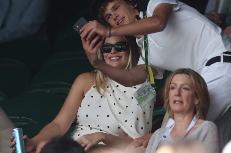 Margot Robbie posa sonriente con un fanático que toma una selfie en Wimbledon. (EFE/EPA/NEIL HALL)

