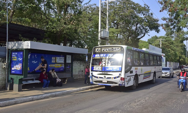 Pasajeros aguardando en una parada de bus, mientras otros se suben una unidad del transporte público.