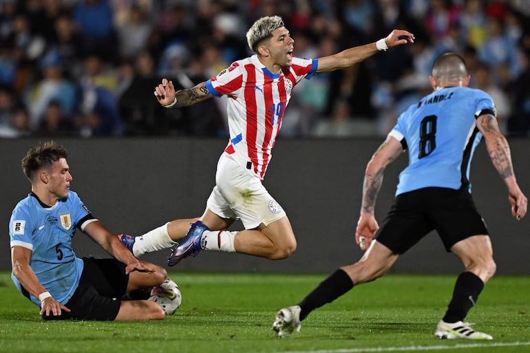 Julio Enciso (c), jugador de la selección de Paraguay, cae al sufrir una falta en el partido ante Uruguay por la séptima fecha de las Eliminatorias Sudamericanas en el estadio Centenario, en Montevideo.