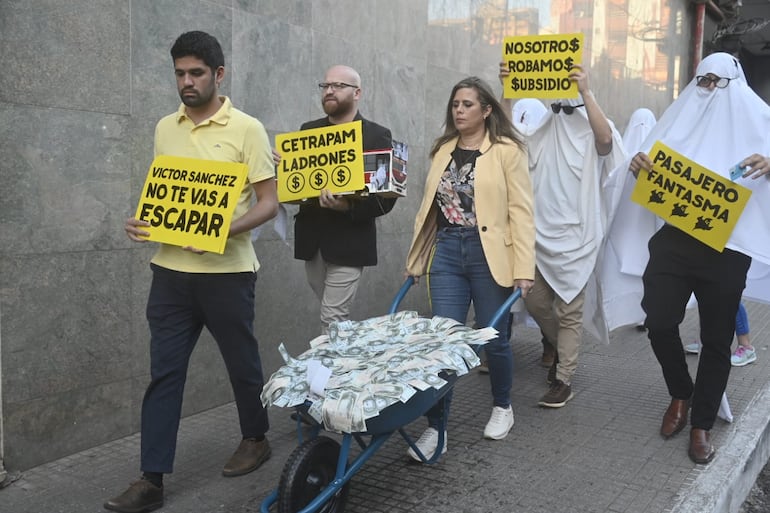 Los candidatos a diputado Juan Grassi y Raúl Benítez y la candidata a senadora Kattya González, todos del Partido Encuentro Nacional (PEN), llegan al Ministerio de Obras Públicas con carteles en contra del empresario del transporte César Ruiz Díaz y el exviceministro Víctor Sánchez. Los acompañan "pasajeros fantasma" y llevan una carretilla cargada de falsos dólares.