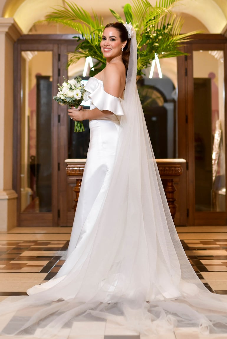 La novia lució hermosa con un vestido confeccionado por Ofelia Otello, de corte strapless en raso blanco con cascada de volados  en la manga y la espalda y un velo de tul plisado.