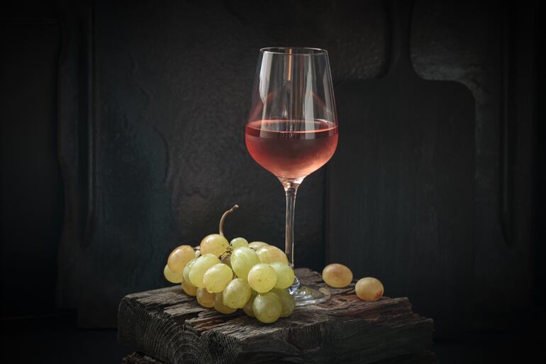 Copa de vino rosado con uvas blancas.