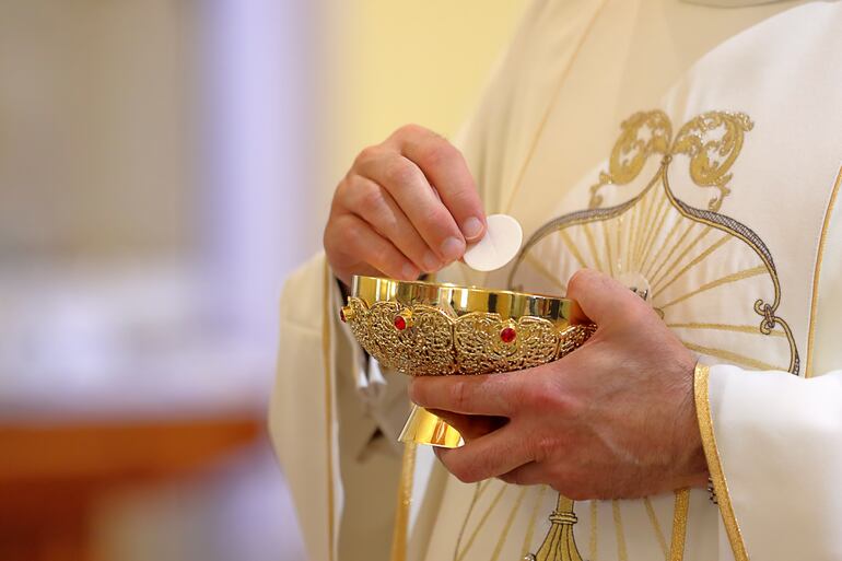 Un cura católico sostiene un cáliz y una hostia.