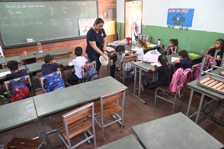 La profesora Isabel Quiñónez derrama agua de un balde en el piso del primer grado, en un intento por refrescar el salón. Los niños faltan, sofocados por el intenso calor.