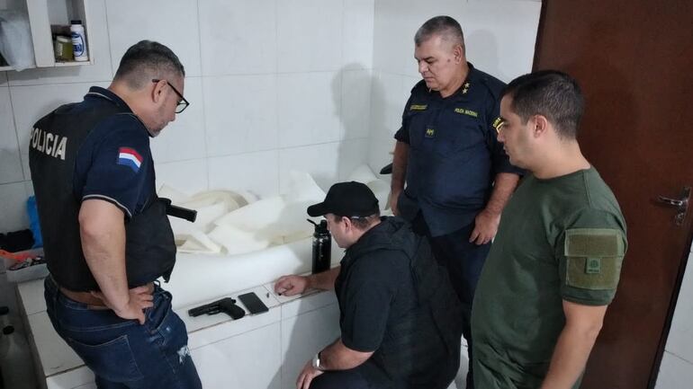 El director de Policía, Feliciano Martínez, y el jefe de Investigaciones, Wilfrido Maldonado, entre otros, observan el arma incautada del abatido Carlos Cabrera Carrera. El fiscal Alcides Giménez es el que está semi sentado.