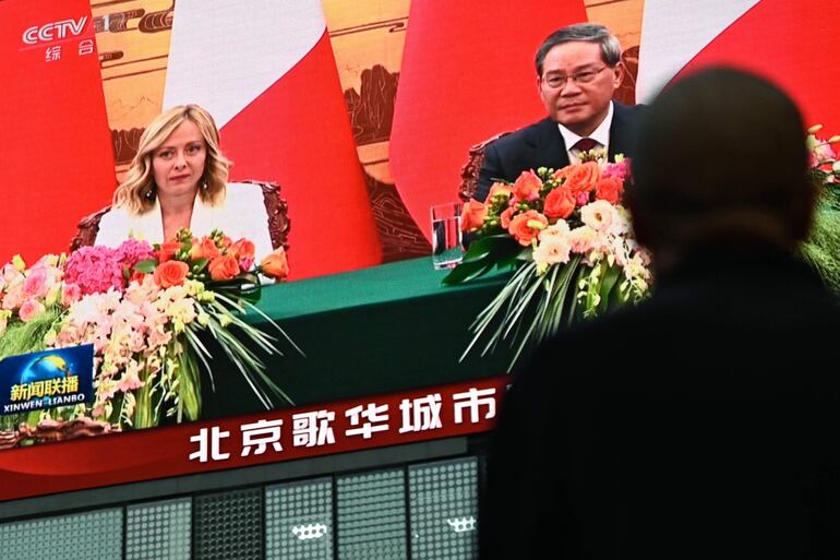 Un hombre mira una pantalla que muestra la cobertura noticiosa de la reunión de la primera ministra de Italia, Giorgia Meloni, con el primer ministro de China, Li Qiang, en Beijing.