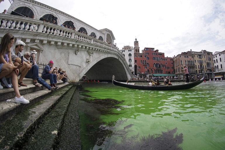 La gente observa una mancha de color verde fosforescenteen el Gran Canal cerca del Puente de Rialto, en Venecia, este domingo. Los bomberos tomaron muestras de agua, mientras que el Prefecto de Venecia convocó una reunión urgente entre las fuerzas policiales de la ciudad, ya que aún se desconoce la causa.