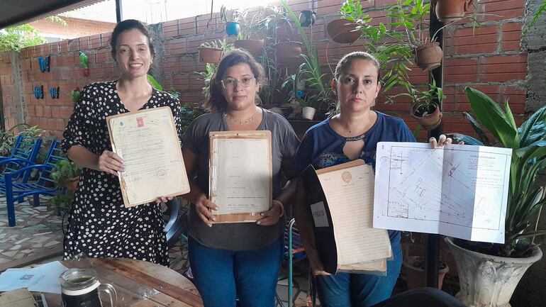 Larissa Ferreira, Cinthia Cáceres y Lourdes Sosa, hijas de los herederos de una propiedad de más de 9 hectáreas invadida en el 2000 en la zona de Pai Ñu Ñemby muestras los documentos originales que avalan la titularidad del terreno. Las mismas exigen desalojo, indemnización y pago por la parte expropiada por el estado en el 2019.