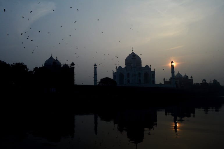 Los pájaros pasan volando junto al Taj Mahal a orillas del río Yamuna durante la puesta de sol de la víspera de Año Nuevo en Agra el 31 de diciembre de 2023.