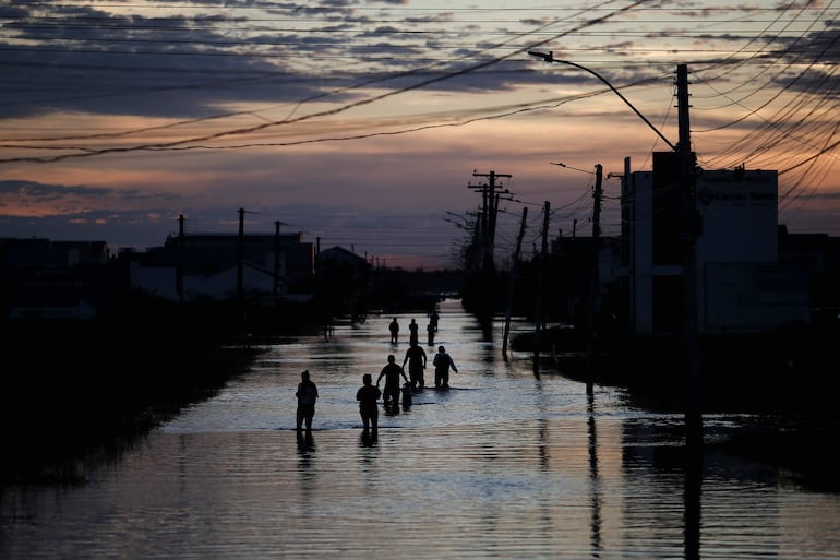 Personas caminan por una calle inundada en Eldorado do Sul, Río Grande del Sur, Brasil, el 9 de mayo de 2024. Equipos se apresuraron el jueves contra reloj para entregar ayuda a las comunidades afectadas por las inundaciones en el sur de Brasil, antes de la llegada de nuevas tormentas pronosticadas para golpear nuevamente la región. Alrededor de 400 municipios han sido afectados por la peor calamidad natural registrada en el estado de Río Grande del Sur, con al menos 107 personas fallecidas y cientos de heridos.