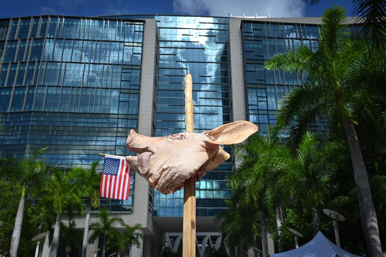 Osmany Estrada (fuera de cuadro) muestra su apoyo con una cabeza de cerdo empalada en una estaca frente al Palacio de Justicia en Miami, antes de la lectura de cargos contra el expresidente Donald Trump.