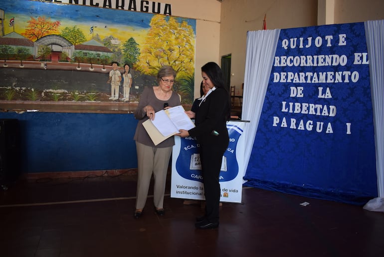 La  historiadora y escritora de Adeap, Margarita Miró, hace entrega de la resolución municipal y copia del proyecto a la directora de la escuela, Eudelia Leiva.