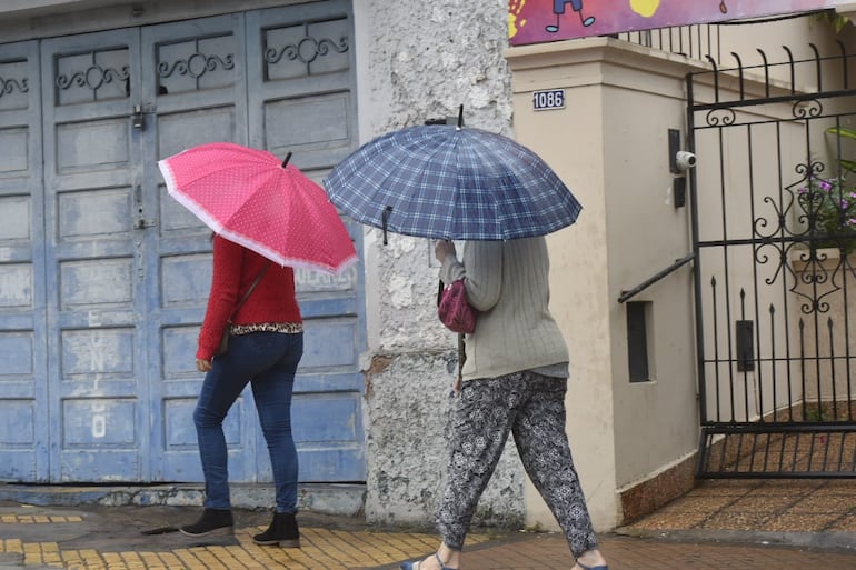 Dos mujeres con paraguas caminan bajo la lluvia en una calle de Asunción.