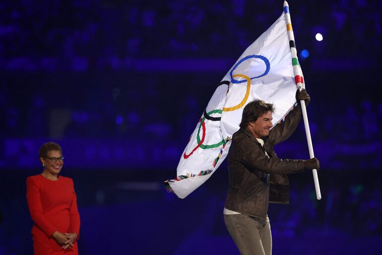 El actor estadounidense Tom Cruise sale con la bandera olímpica frente a la alcaldesa de Los Ángeles, Karen Bass, y a la gimnasta estadounidense Simone Biles durante la ceremonia de clausura de los Juegos Olímpicos de París 2024 en el Stade de France, en Saint-Denis, en el afueras de París.