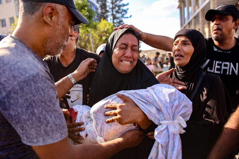 Una mujer lleva el cuerpo sin vida de un niño fallecido en el bombardeo israelí a una escuela donde se refugiaban personas desplazadas, este sábado en la Ciudad de Gaza.