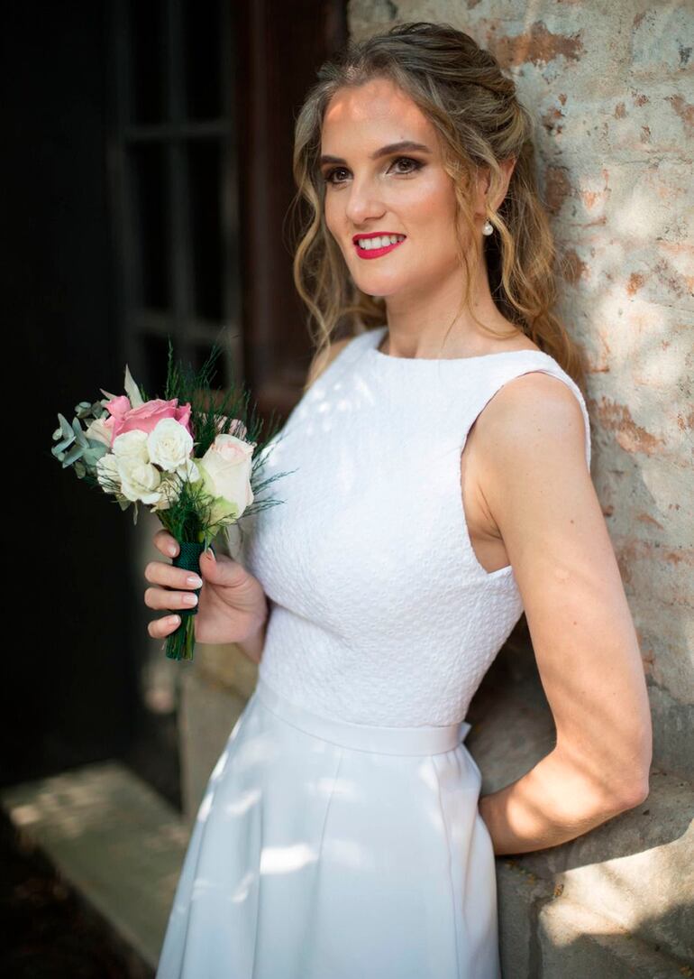 La novia lució muy sofisticada y fresca, ella llevó un vestido blanco clásico diseñado y confeccionado por Laura Benítez y portó un delicado ramito hecho con rosas blancas y rosadas, también con gipsofilas. El tocado fue trabajado por Zuni Vega.