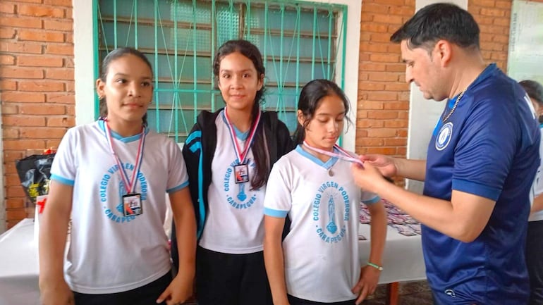 El profesor Milciades Ruíz Díaz, entrega la medalla a las ganadoras del nivel escolar básico, Maira Sánchez, Ada Galeano y Lizet Sánchez.