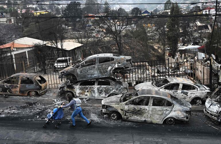 Una mujer con su bebé pasa junto a vehículos quemados después de un incendio forestal en Quilpue, región de Valparaíso, Chile, el 4 de febrero de 2024.
