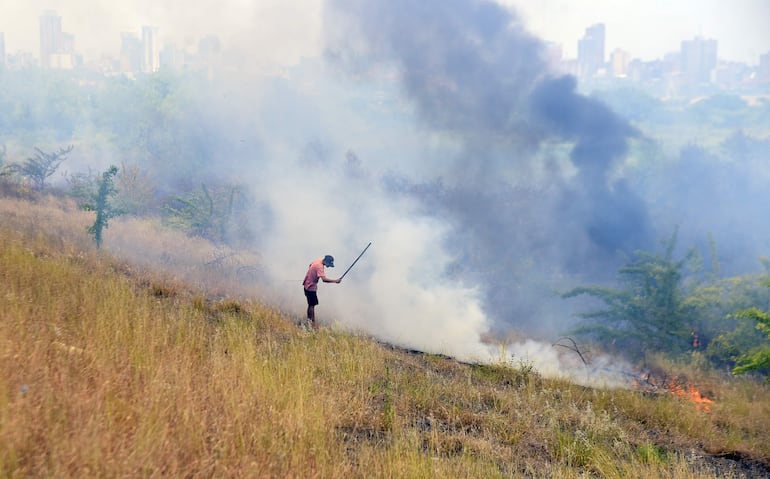 Un poblador de la zona, intenta aplazar el fuego que inició en el banco San Miguel y se extendió hasta la Costanera de Asunción.