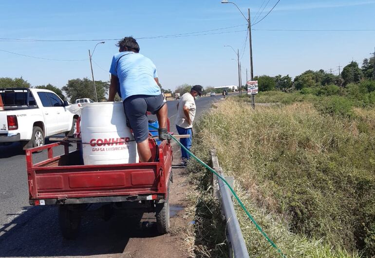 Un poblador de la zona de San Antonio  carga su tambor en una conexión clandestina mediante una manguera.