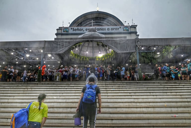 Feligreses se resguardan de la lluvia bajo el techo de la explanada de la Basílica de Caacupé.