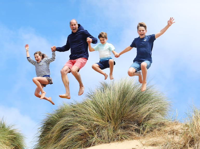 Carlota, William, Luis y Jorge saltan tomados de las manos sobre una duna de arena.