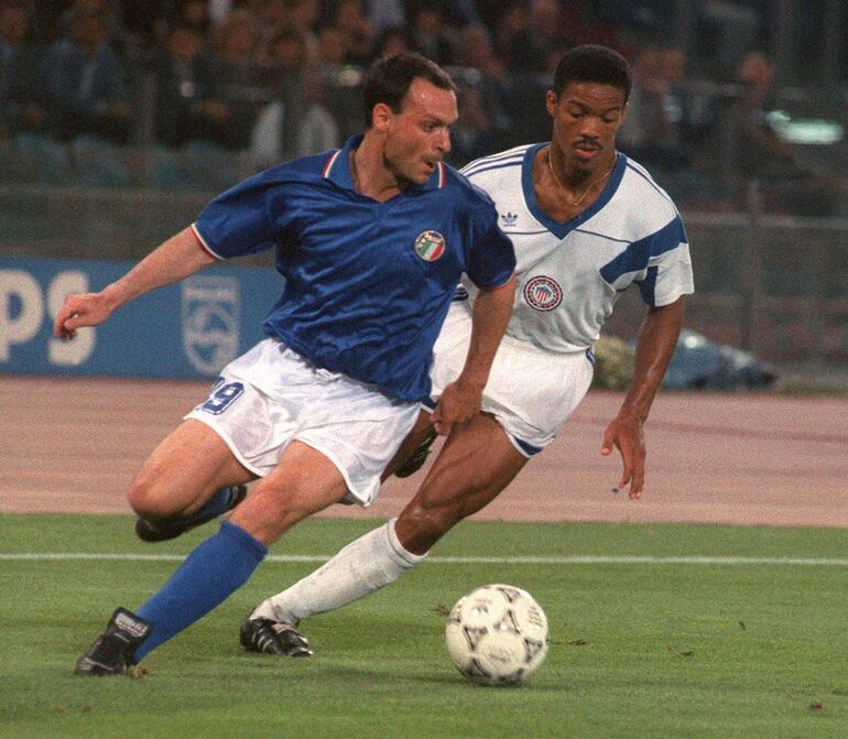 (FILES) Italian forward Salvatore Schillaci (L) tries to control the ball under pressure from US defender Jimmy Banks during the World Cup first round soccer match between Italy and the United States 14 June 1990 in Rome. Former Italy striker Salvatore "Toto" Schillaci, most famous for being top scorer at the 1990 World Cup, died on September 18, 2024 at the age of 59. Juventus were among Italy's football clubs to pay tribute to Schillaci, who became an icon for his unexpected goalscoring exploits at his country's home World Cup, simply saying "Ciao Toto" on social media with a picture of him in a Juve shirt. (Photo by STAFF / AFP)