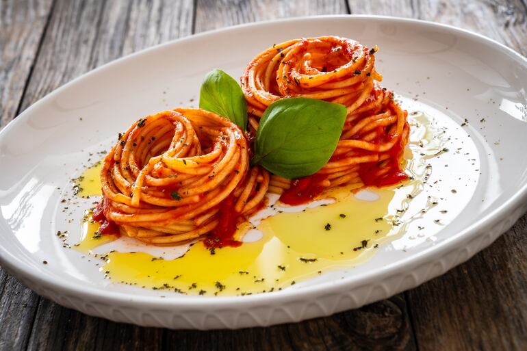 Un plato blanco con dos nidos de fideos cubiertos son salsa de tomate y aceite de oliva