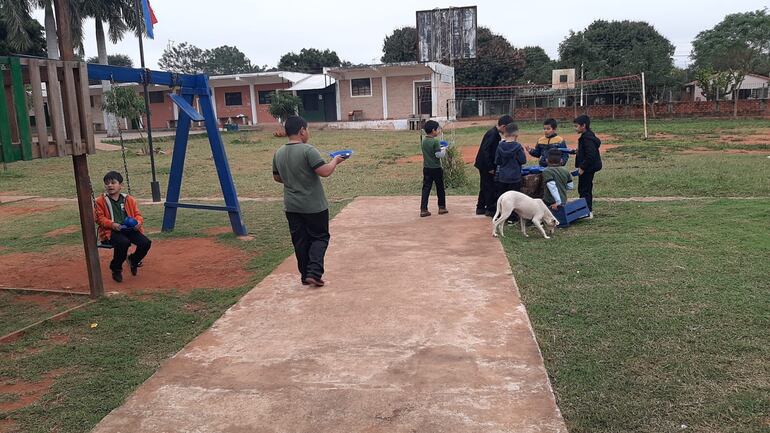 En una hamaca un niño sentado, otro casi en frente recorre con su plato en mano, y en otro grupo varios niños almuerzan de pie, sentados de rodillas.