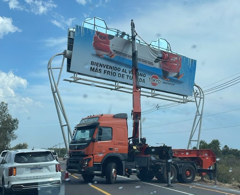 Una grúa que tiene las siglas M.O.P.C (Ministerio de Obras Públicas y Comunicaciones) acompaña la instalación de carteles publicitarios.