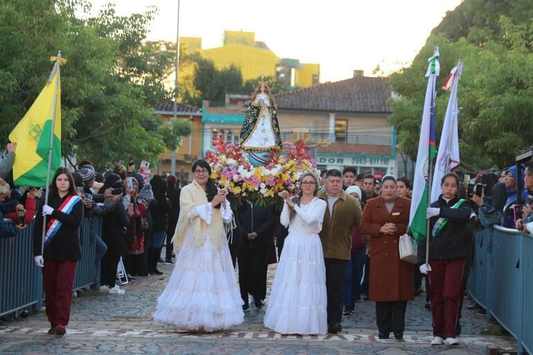 La figura de la madre común de los paraguayos llevada en andas por devotas vestidas con trajes típicos. 
