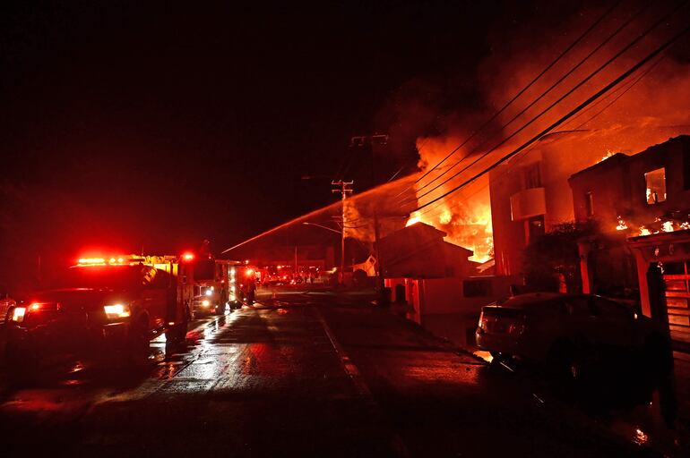 Los bomberos trabajan para apagar un incendio mientras las casas arden a lo largo de la Pacific Coast Highway durante el incendio de Palisades en Malibú, California.